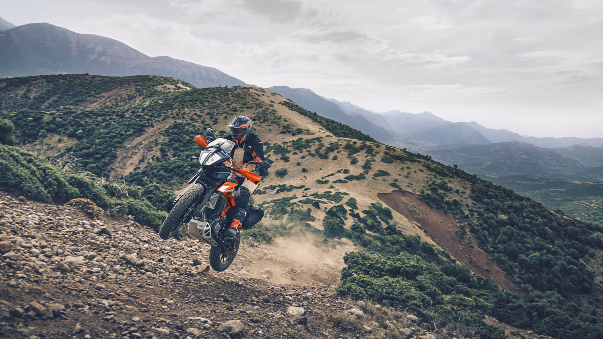 A motorcycle rider on the KTM 390 Adventure as it gets airborn on a hilltop dirt track.